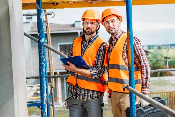 Bei costruttori fiduciosi con appunti in piedi in cantiere — Foto stock