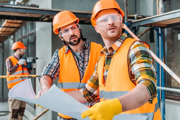 Handsome thoughtful builders with blueprint looking away — Stock Photo