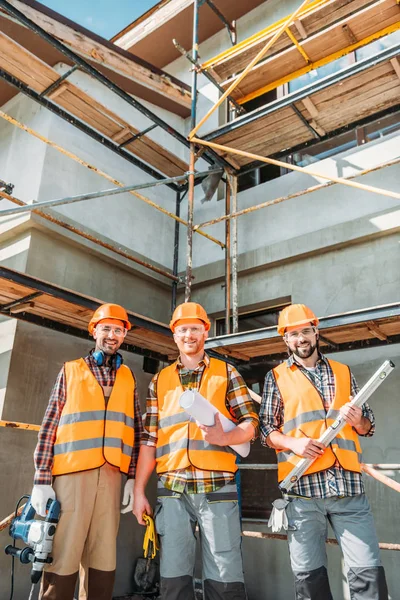 Grupo de construtores sorrindo equipados olhando para a câmera no local de construção — Fotografia de Stock