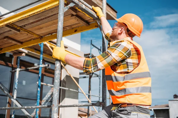 Hermoso constructor escalando en andamios en el sitio de construcción - foto de stock