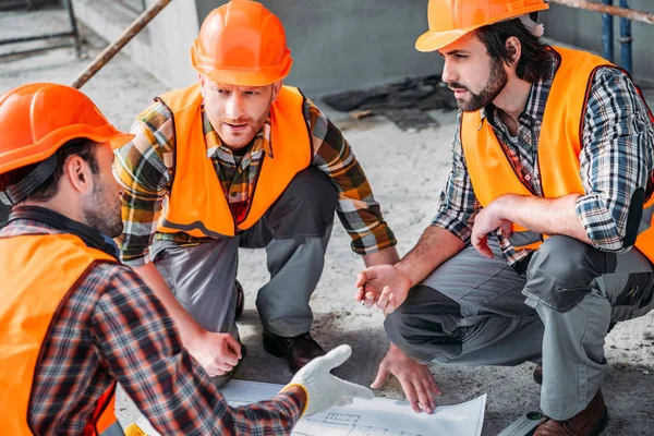 Nahaufnahme einer Gruppe selbstbewusster Bauarbeiter, die sich über den Bauplan unterhalten — Stockfoto