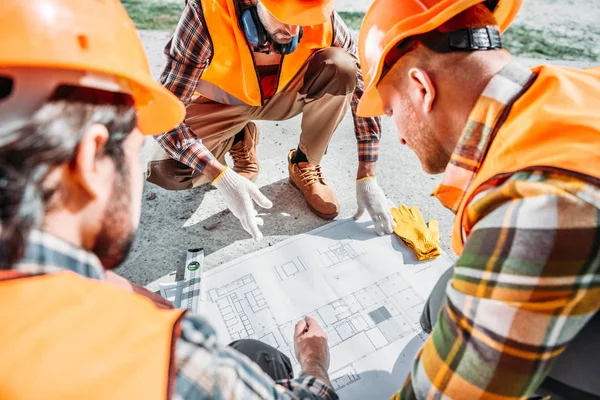 Primer plano de grupo de constructores en sombreros duros tener una conversación sobre el plan de construcción - foto de stock