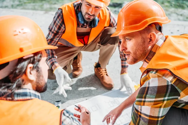 Nahaufnahme einer Gruppe von Bauarbeitern mit harten Hüten, die sich über Baupläne unterhalten — Stockfoto