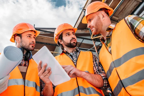 Groupe de constructeurs utilisant une tablette numérique sur le chantier de construction — Photo de stock
