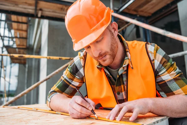 Apuesto constructor usando cinta métrica y lápiz en el sitio de construcción - foto de stock