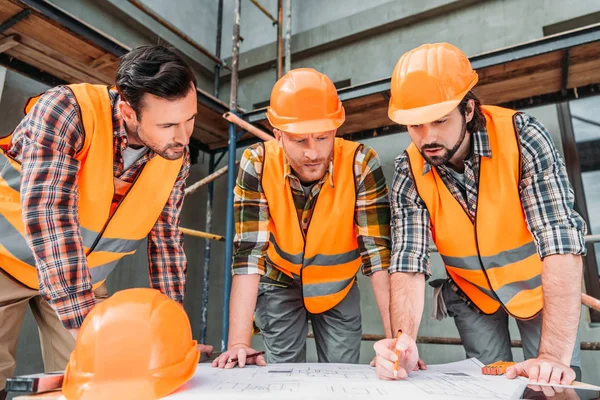 Grupo de constructores confiados mirando el plan de construcción en el sitio de construcción - foto de stock