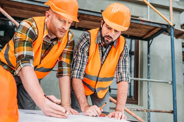Les constructeurs confiants dessinent le plan de construction sur le chantier — Photo de stock