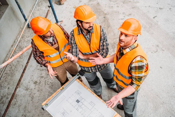 Visão de alto ângulo do grupo de construtores confusos discutindo o plano de construção no canteiro de obras — Fotografia de Stock