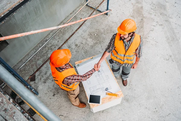 Высокий угол обзора строителей пожимающих руки на строительной площадке — стоковое фото