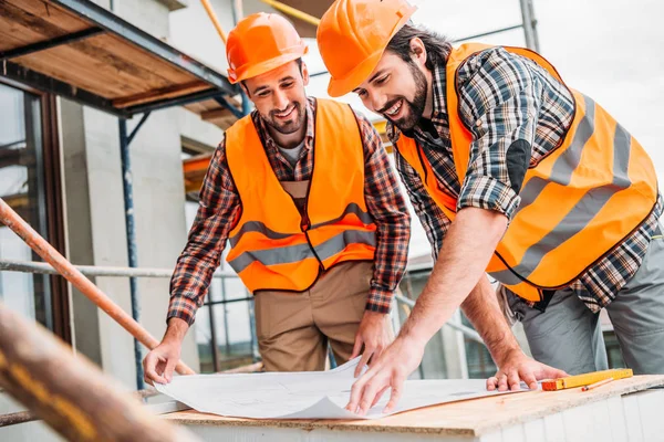 Handsome smiling builders looking at construction plan — Stock Photo