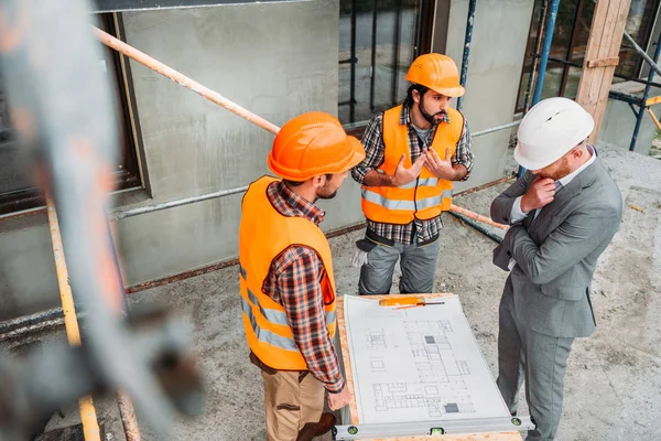 Visão de alto ângulo de construtores confusos e arquiteto discutindo plano de construção no canteiro de obras — Fotografia de Stock