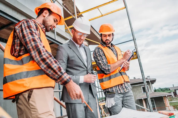 Bottom view of builders and architect discussing blueprint at construction site — Stock Photo