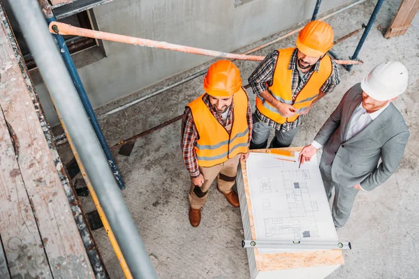 Blick aus der Vogelperspektive auf lächelnde Bauarbeiter und Architekten, die den Bauplan auf der Baustelle diskutieren — Stockfoto