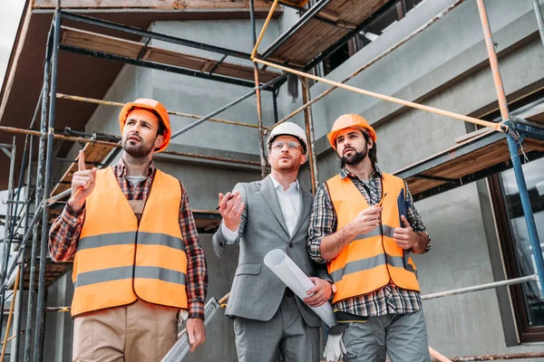 Construtores e arquiteto olhando para longe na frente do canteiro de obras — Fotografia de Stock