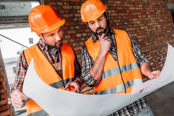 Nachdenkliche, selbstbewusste Bauarbeiter arbeiten mit Bauplan auf Baustelle — Stockfoto