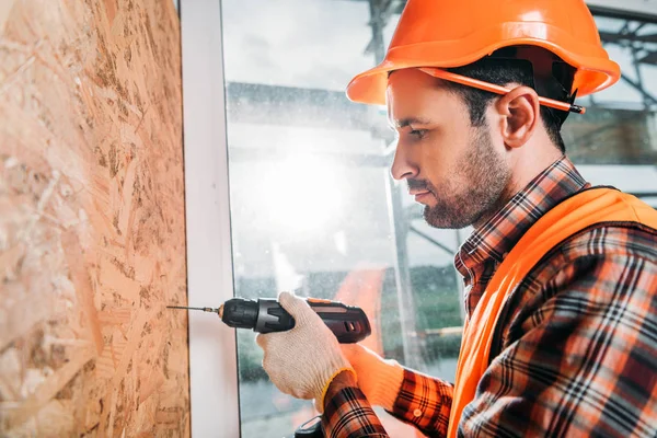 Vista laterale del bel costruttore utilizzando trapano elettrico portatile — Foto stock