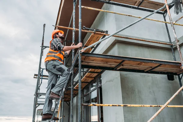 Handsome builder climbing on scaffolding at construction site — Stock Photo