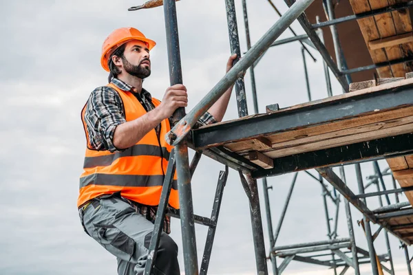 Bearded builder climbing on scaffolding at construction site — Stock Photo