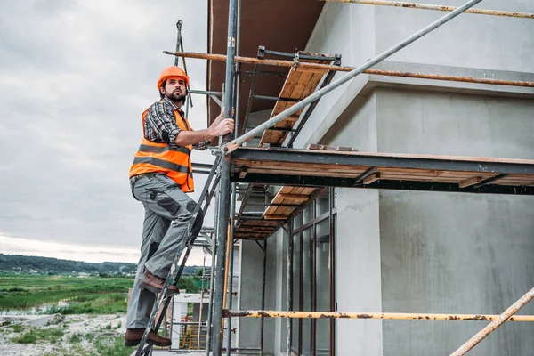 Construtor subindo em andaimes no local de construção e olhando para longe — Fotografia de Stock