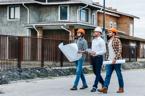 Group of architects walking by building street with blueprints — Stock Photo