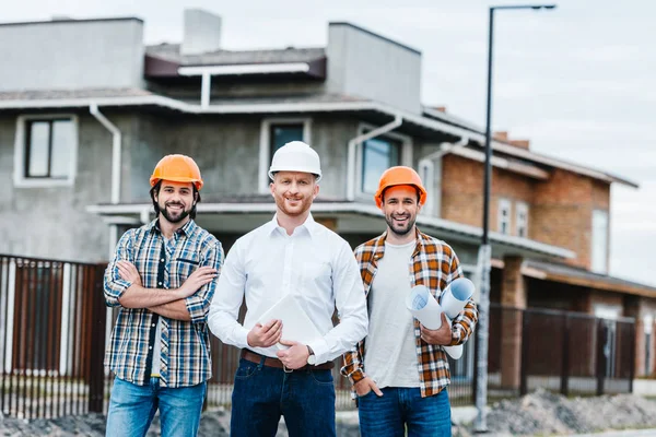 Group of smiling architects in hard hats looking at camera on building street — Stock Photo