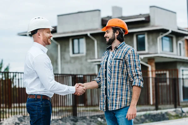 Arquitectos guapos estrechando las manos en el sitio de construcción - foto de stock