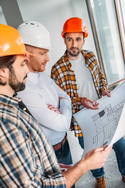 Group of architects with blueprint having conversation inside of constructing building — Stock Photo