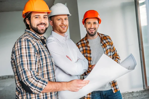 Group of architects with blueprint inside of constructing building looking at camera — Stock Photo