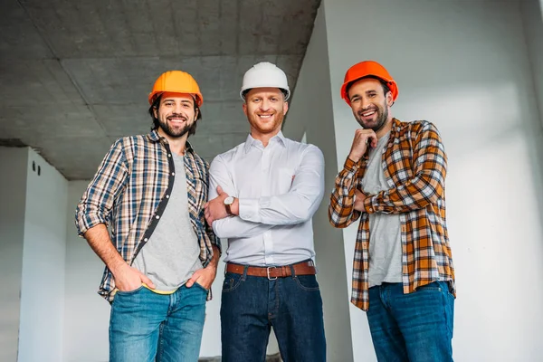 Groupe d'architectes souriants à l'intérieur de la construction du bâtiment regardant la caméra — Photo de stock