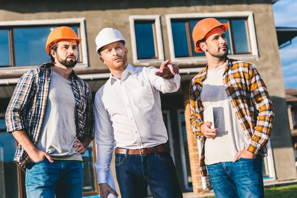 Grupo de arquitectos guapos teniendo conversación y señalando en algún lugar - foto de stock