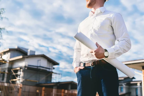 Cropped shot of architect in white shirt with blueprint standing at yard in front of building house — Stock Photo