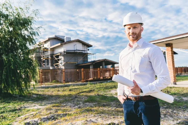 Handsome architect in white shirt with blueprint standing at yard in front of building house — Stock Photo