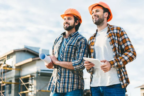 Architects with blueprint and tablet looking away at construction site — Stock Photo