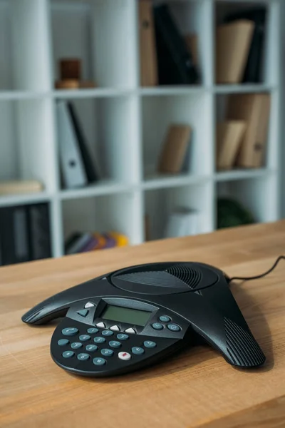 Speakerphone on wooden table at office with blurred bookshelves on background — Stock Photo