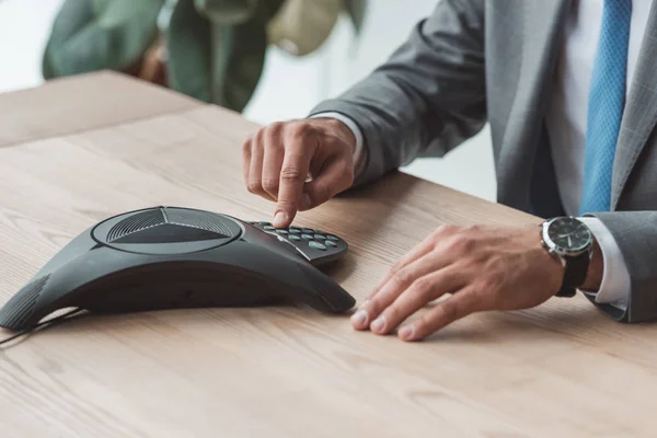 Cropped shot of businessman in suit pushing button of speakerphone at workplace — Stock Photo