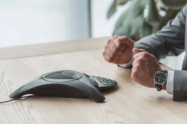 Cropped shot of businessman sitting in front of conference phone and making fists at office — Stock Photo