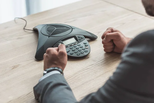 Обрезанный снимок разъяренного бизнесмена, сидящего перед телефоном и сжимающего кулаки в офисе — стоковое фото