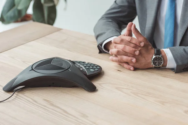 Colpo ritagliato di uomo d'affari seduto sul posto di lavoro con telefono conferenza — Foto stock