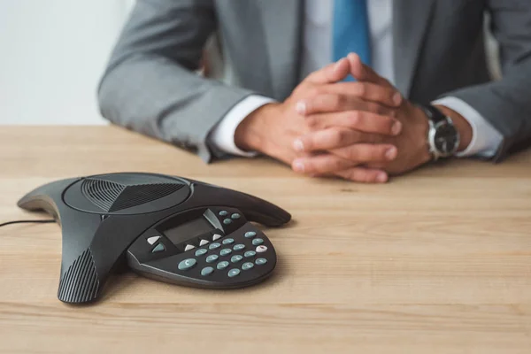 Cropped shot of businessman sitting behind conference phone on table at office — Stock Photo