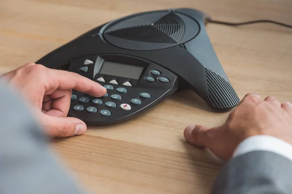 Tiro cortado de empresário empurrando botão de telefone conferência na mesa de madeira no escritório — Fotografia de Stock