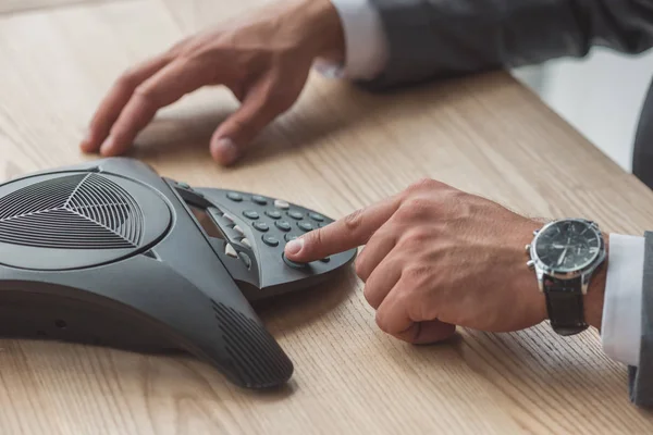 Cropped shot of businessman in suit pushing button of conference phone on table at office — Stock Photo