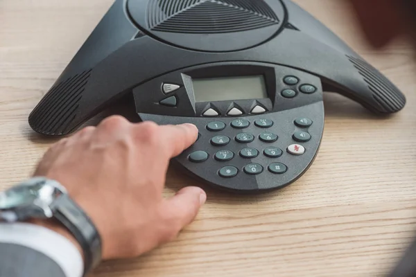 Cropped shot of businessman with stylish wristwatch pushing button of conference phone on table at office — Stock Photo