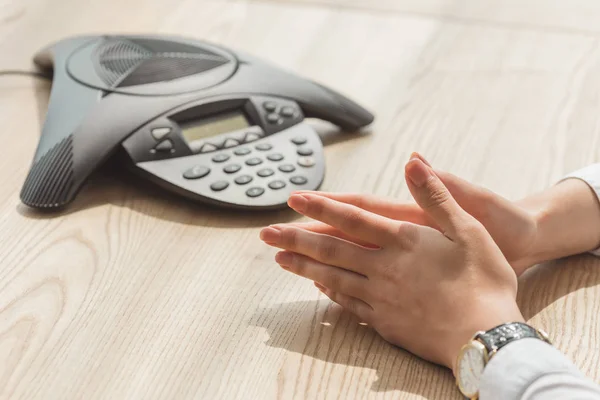 Plan recadré d'une femme d'affaires assise devant un téléphone de conférence sur une table en bois — Photo de stock