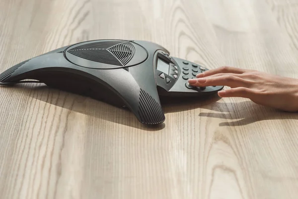 Cropped shot of businesswoman pushing button of speakerphone on wooden table — Stock Photo