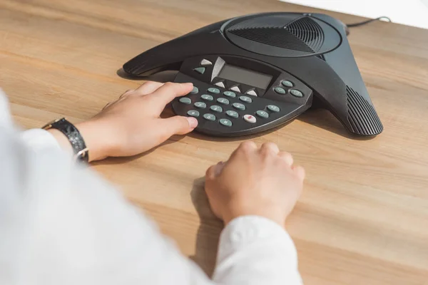 Cropped shot of businesswoman pushing button of conference phone on table at office — Stock Photo