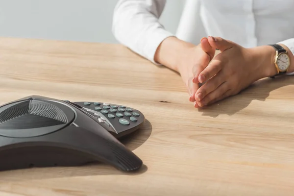 Cropped shot of businesswoman in white shirt sitting in front of conference phone on table at office — Stock Photo