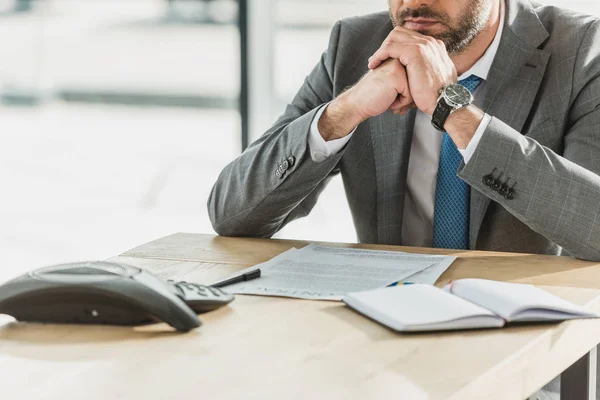 Tiro cortado de homem de negócios sentado no local de trabalho com telefone conferência na mesa no escritório — Fotografia de Stock