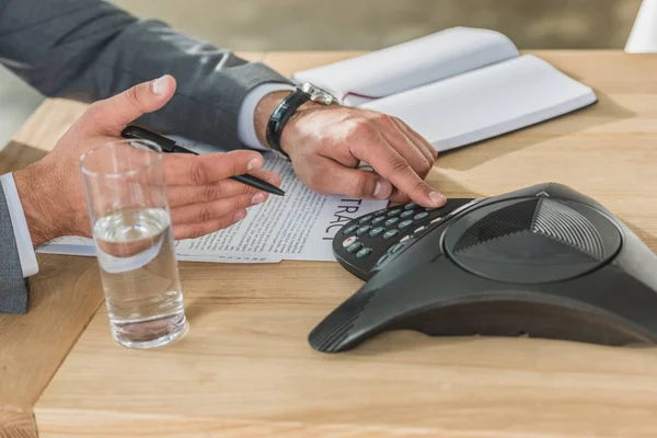 Обрезанный снимок бизнесмена с помощью конференц-телефона на столе в офисе — стоковое фото