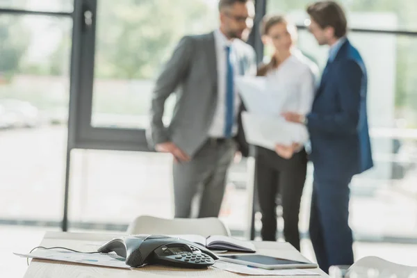 Close-up shot of conference phone with blurred business people on background at office — Stock Photo