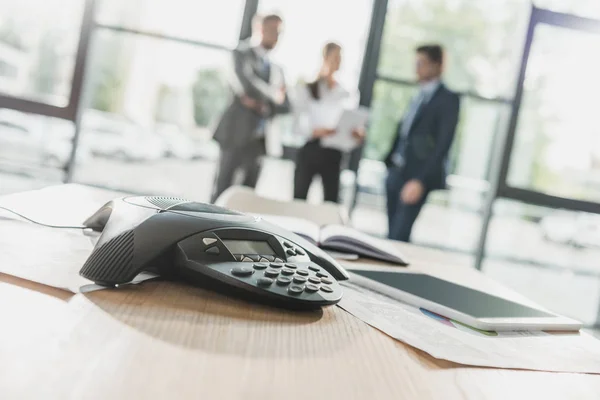 Close-up shot of conference phone with blurred business people on background at modern office — Stock Photo
